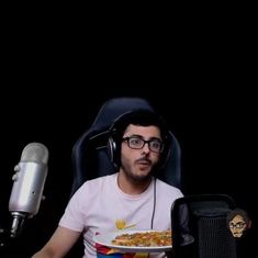 a man wearing headphones sitting in front of a microphone and holding a plate of food