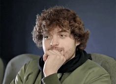 a man with curly hair sitting in a chair looking at the camera while wearing a scarf