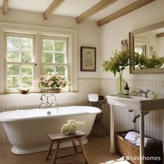 a white bath tub sitting next to a window in a bathroom with wooden beams on the ceiling