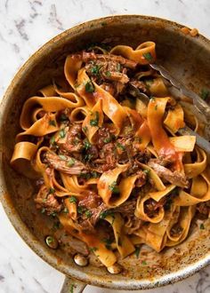 a bowl filled with pasta and meat on top of a marble countertop next to a fork