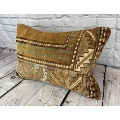 a brown and green decorative pillow sitting on top of a wooden floor next to a brick wall