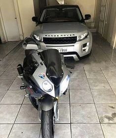 a silver car parked next to a motorcycle in a room with tile flooring and white walls