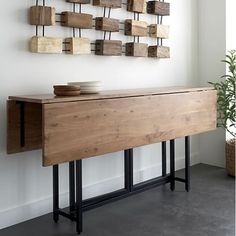 a wooden table with metal legs and a bowl on it in front of a white wall