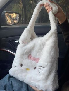 a person holding up a white hello kitty bag in their hand while sitting in the back seat of a car