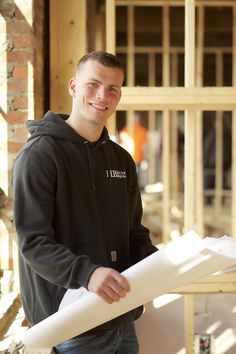 a young man holding a blueprint while standing in front of a building under construction