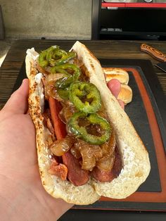 a hand holding a hot dog with onions and peppers on it, in front of buns