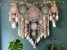 a wall hanging with pink and white dream catchers on it's side next to a potted plant