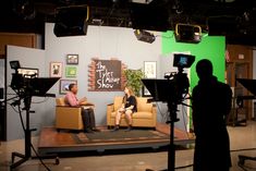 two people are sitting in chairs on a set with green screen behind them and camera equipment