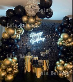 a birthday party with balloons and black and gold decorations on the front wall, along with an arch