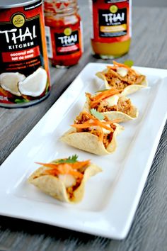 some tacos are sitting on a plate next to cans of thai kitchen seasoning