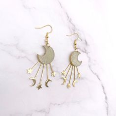 Channel the Celestial Glow with Golden Crescent Moon and Star EarringsEnchant any outfit with these magical moon earrings. Each earring features a delicate crescent moon charm adorned with stars, gracefully dangling from gleaming gold-colored hook wires.Details:Length: 2 inchesWidth: 1.5 inchesMaterial: Polymer clay, gold colored brass charms and findingsClosure: Secure pushback closureCrafted with lightweight polymer clay, these earrings measure approximately 2 inches long and 1.5 inches wide, Whimsical Gold Earrings With Moon Charm, Celestial Crescent Earrings For Party, Celestial Moon Earrings For Party, Celestial Moon Shape Party Earrings, Moon-shaped Celestial Party Earrings, Celestial Moon-shaped Party Earrings, Crescent Moon Charm Earrings For Party, Crescent Moon Charm Party Earrings, Cottage Core Pastel