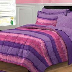 a bed with purple and pink bedspreads in a room next to a window