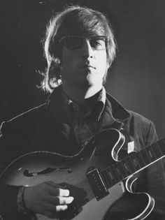 a black and white photo of a man with glasses playing an electric guitar in front of a microphone