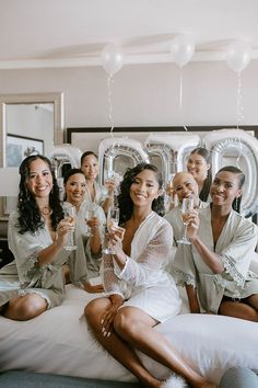 a group of women sitting on top of a bed holding wine glasses in their hands