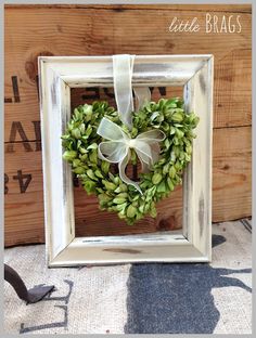 a white frame with a green wreath hanging from it's side on a table