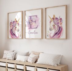 two framed unicorn pictures hang on the wall above a bench with pillows and storage bins