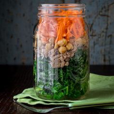 a glass jar filled with vegetables and meats on top of a green napkin next to a wooden table