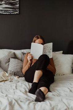 a woman laying on top of a bed reading a book