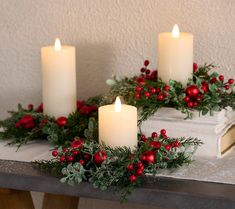 three lit candles on a table with holly and berries