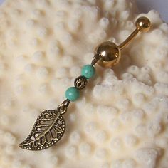 a gold belly ring with green beads and a leaf dangling from it's side