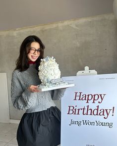 a woman holding a cake in front of a happy birthday sign