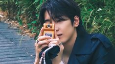 a young man taking a photo with his cell phone while sitting in front of some bushes