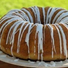 a bundt cake with icing sitting on a white plate in front of a green field