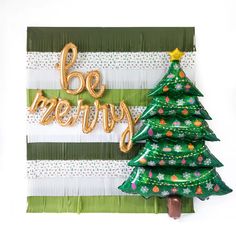 a green christmas tree with gold foil balloons and the words be merry written on it