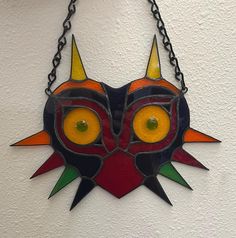 a colorful mask hanging from a chain on a wall with eyes and horns painted on it