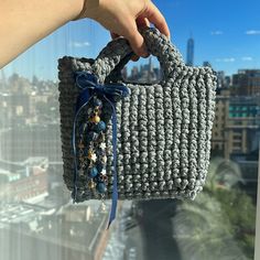 a hand holding a gray crocheted purse over a cityscape