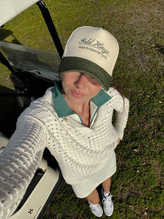 a woman sitting on the ground next to a golf cart wearing a hat and sweater