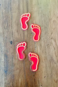 three pink footprints on a wooden surface with one being cut out to look like it's feet