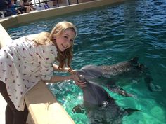 a girl petting two dolphins in the water