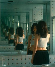 two women standing in front of a bathroom mirror looking at their own reflection on the wall