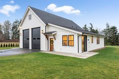 a white house with black garage doors and windows on the front lawn, surrounded by green grass