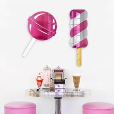 two pink stools are next to a round table with ice cream pops on it