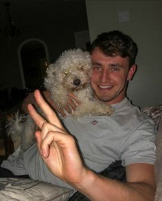 a man sitting on a couch holding a dog in his lap and making the peace sign