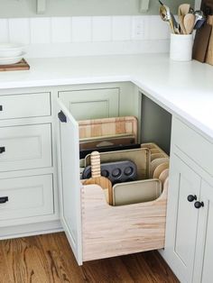 an open drawer in the middle of a kitchen with white cabinets and wood flooring