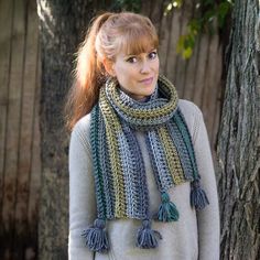 a woman standing in front of a tree wearing a scarf with tassels on it