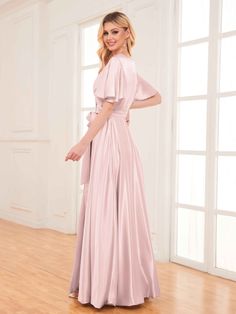 a woman in a long pink dress standing on a wooden floor with her hands behind her back