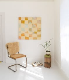 a white room with a chair and a painting hanging on the wall next to a potted plant