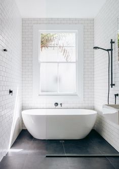 a white bath tub sitting next to a window in a bathroom with black tile flooring