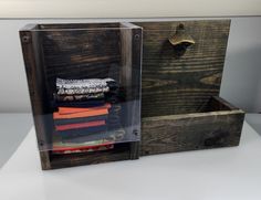 an open wooden box with folded clothes in it sitting on a table next to a wall hook