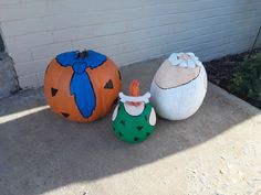 three painted pumpkins sitting next to each other on the cement ground in front of a brick wall