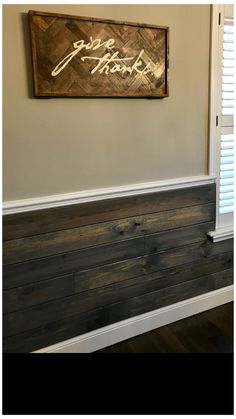 a wooden sign hanging on the side of a wall next to a window with shutters