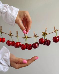 a woman's hands holding cherries on a clothes line with one hand reaching for the cherries