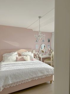 a bedroom with pink walls, white bedding and a chandelier hanging from the ceiling