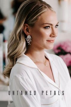 a woman with blonde hair wearing earrings and a white shirt is looking off to the side