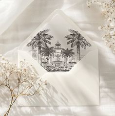 an envelope with a drawing of palm trees and a building in the middle is surrounded by white flowers