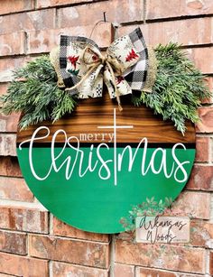 a merry christmas sign hanging on the side of a brick building with evergreen wreaths